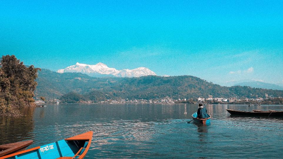 person riding on blue boat on body of water viewing mountain under blue and white sky